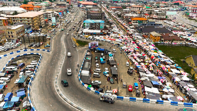 Aerial view of Isaac Boro Park bustling with cars and traders under colorful umbrellas, a vibrant intersection of commerce and motion, Abali Park, Port Harcourt, Nigeria.