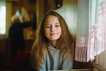 A portrait of a teenage girl sitting at a table in a village home. Her expression is calm and natural, capturing the quiet simplicity of rural life.