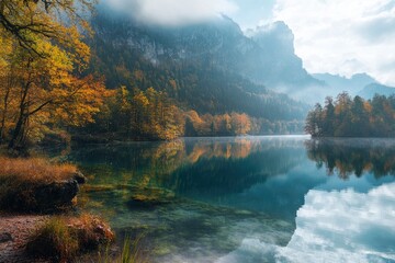 A picturesque autumn landscape with a lake shore under a mountain and trees with yellow leaves. The surface of the lake reflects everything around.