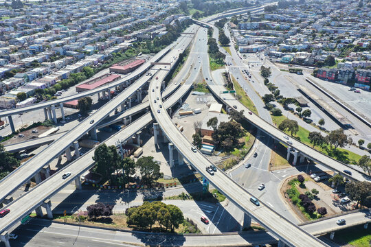 Aerial view of a complex highway interchange system with numerous overpasses and underpasses cutting through a densely populated urban area, San Francisco, California, United States.