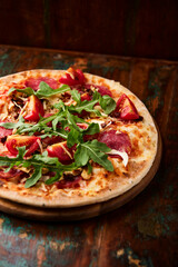 Pizza with ham, salami, tomatoes and mozzarella cheese. Rustic wooden background. Soft focus. Close up.	