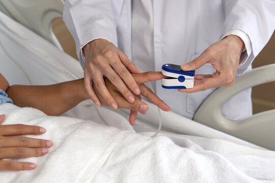 A healthcare professional is using a fingertip pulse oximeter on a patient’s finger in a hospital room. This procedure is crucial for assessing respiratory health and blood oxygen level. Close up