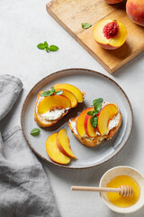 Toasted bruschetta with peach, nectarine, cream cheese or ricotta and honey on a plate on a light background