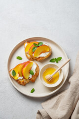 Toast bruschetta with peach, nectarine, cream cheese or ricotta and honey on a plate on a light background