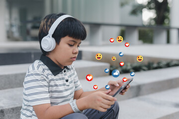 Asian boy using smartphone with social media emoji icons, representing online communication, digital lifestyle, like, love, happy, social network interaction, and modern internet technology concept.