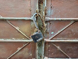 Old rusty unlocked padlock hanging on a weathered and corroded metal gate. A vintage grunge texture symbolizing insecurity, access, or forgotten secrets.