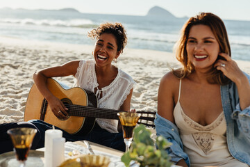 Women enjoying music and laughter during a sunny beachside picnic