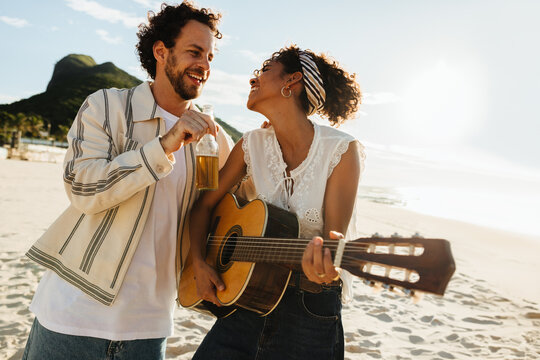 Young couple enjoying guitar music and beer at a beach sunset