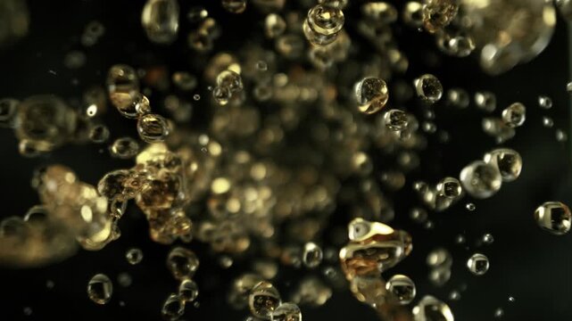Super Slow Motion Shot of Flying Golden Liquid Drops Towards Camera on Black Background at 1000fps.