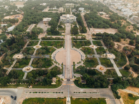 Aerial view of a grand, symmetrical parkway cutting through lush greenery towards a palatial building, framed by the city's edge, Nouakchott, Ksar, Mauritania.