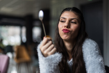 Young woman in a cozy sweater presenting a spoon in a café setting