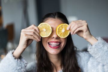 Joyful woman with braces holding lemon slices in a playful pose