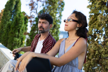 Casual outdoor interaction between two friends enjoying a sunny day in a park setting, with trees...