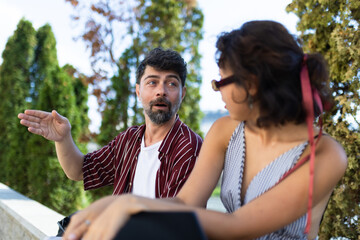 Casual conversation between friends outdoors on a sunny day, with a relaxed atmosphere and green...