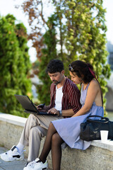 Couple working together on a laptop outdoors, enjoying a sunny day while discussing new ideas and...