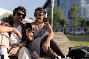 Trendy friends relaxing outdoors wearing headphones and sunglasses while sharing music from a...