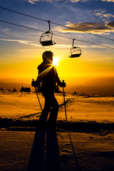 Silhouette of skier at sunset on snowy mountain with ski lifts above