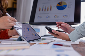 Business people analyzing financial charts and graphs displayed on a digital tablet and computer screen, using a calculator to perform calculations and make informed decisions