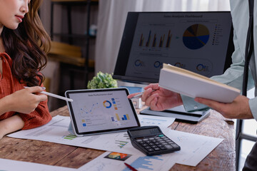 Business colleagues discussing sales performance while analyzing charts and graphs on a digital tablet and computer during a collaborative meeting for growth strategies