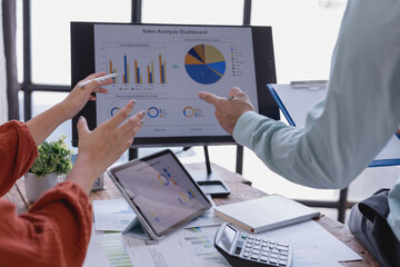 Business team working together analyzing sales data using computer, tablet, and documents, discussing company performance and making strategic decisions based on market trends