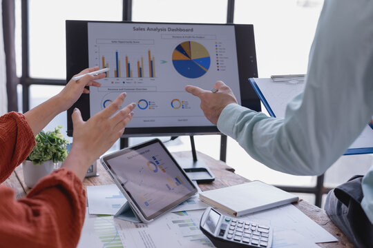 Business team working together analyzing sales data using computer, tablet, and documents, discussing company performance and making strategic decisions based on market trends