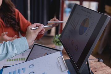 Business colleagues discussing financial charts and graphs using a computer, tablet, and documents, analyzing sales performance and market trends during a collaborative meeting