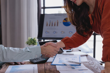 Business partners shaking hands over a wooden table with financial charts, graphs and electronic devices, celebrating successful data analysis and strategic planning