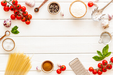 Spaghetti with ingredients for cooking Italian pasta - tomatoes and basil with garlic - on a white wooden background, top view. Flat lay
