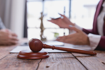 Wooden gavel resting on a sound block atop a desk, with a blurred lawyer providing counsel to a...