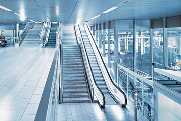 Empty escalators inside airport hallway with large windows, no people
