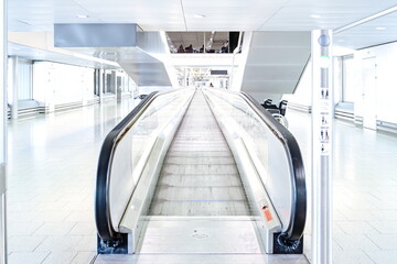 Empty escalators inside airport hallway with large windows, no people