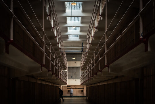 View of stark Alcatraz prison cell blocks stretch into the dim light, casting long shadows in a historic penitentiary, San Francisco, California, United States.