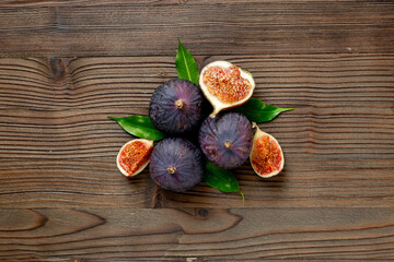 Purple ripe figs fruit and slices with green leaves top view on a wooden background