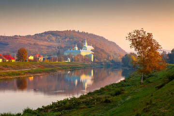 Fototapeta premium mukachevo, ukraine - 06 nov, 2015: urban landscape with river and trees in autumn. reflection of a monastery in the distance. beautiful travel destination of transcarpathia