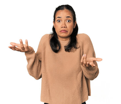 Young Filipina woman doubting and shrugging shoulders in questioning gesture.