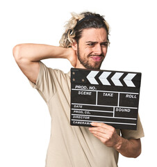 Young man with clapperboard in studio touching back of head, thinking and making a choice.