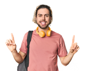 Young student with backpack and headphones indicates with both fore fingers up showing a blank space.