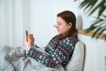 Girl using smart phone while lying on bed in bedroom