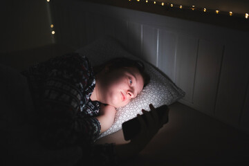 Girl using smart phone while lying on bed in bedroom