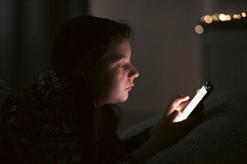 Girl using smart phone while lying on bed in bedroom