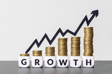 Stacks of coins with increasing chart arrow on top of a GROWTH message on cube blocks. Copy space