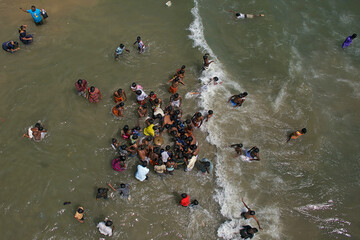 Puducherry, India - 28 February 2010: Aerial view of a lively scene where people gather and frolic in the ocean's embrace, creating a vibrant contrast against the sandy shore.