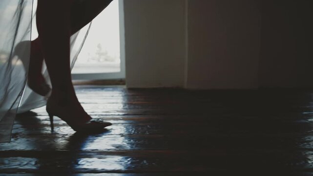 black silhouette close-up feet body part woman sexy fashion model walking dressed in classic high heel shoes long legs white silk dress. Girl go foot step old wooden floor. dark room window light 4k