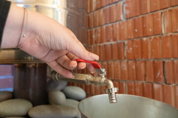 A person is carefully opening a faucet that has a bright red handle