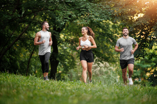 Friends enjoy running together on a sunny day in a lush green park during early evening hours - Powered by Adobe
