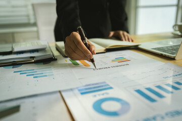 A businessman calculates finances using a calculator, analyzing charts and graphs on documents, while working with laptop and smartphone in office.