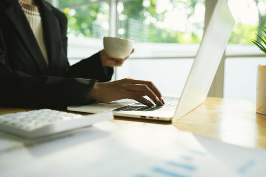 A businessman calculates finances using a calculator, analyzing charts and graphs on documents, while working with laptop and smartphone in office.