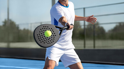 Cropped view of men swinging a padel racket to strike a ball in motion inside a padel court