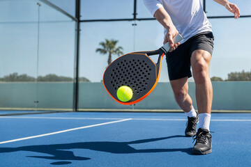 low angle view of men swinging a padel racket to strike a ball in motion inside a padel court