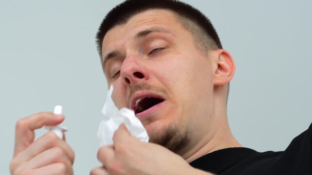 A guy sprays medicine into his nose and wipes his nose with a napkin.
Runny nose and cold.
Allergic reaction in a guy.
Respiratory seasonal diseases and weakened immunity